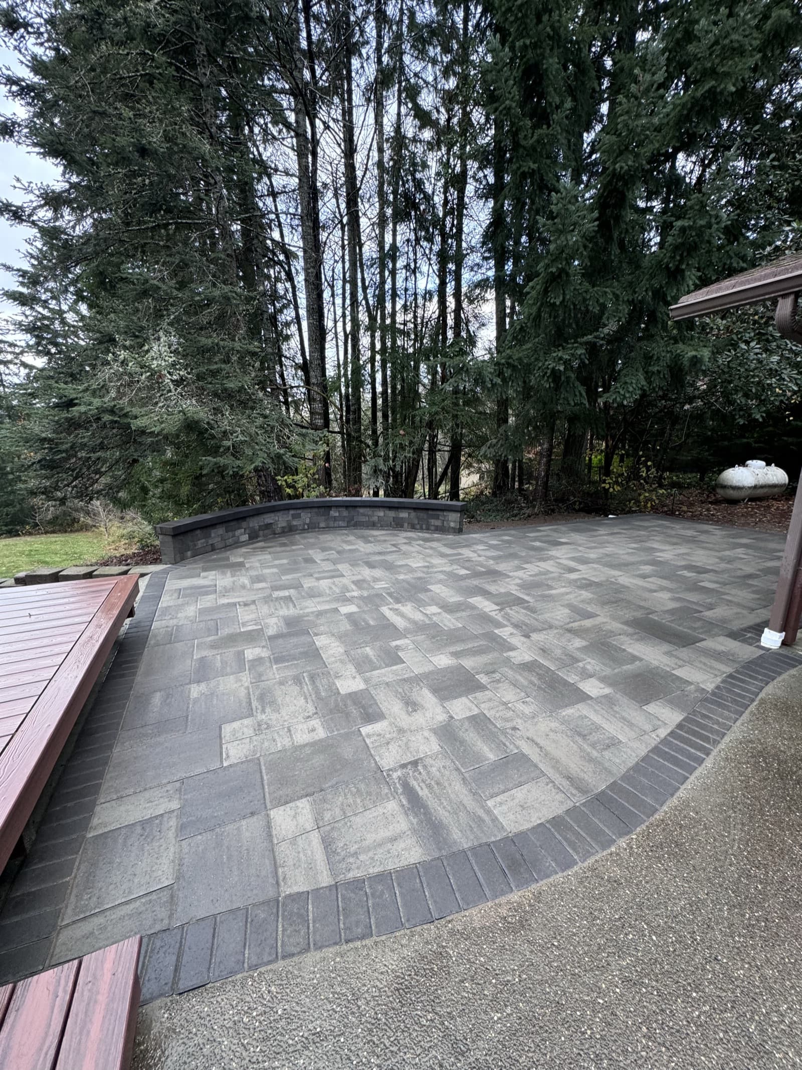 Curved paver patio with stone seating wall surrounded by Pacific Northwest evergreen trees